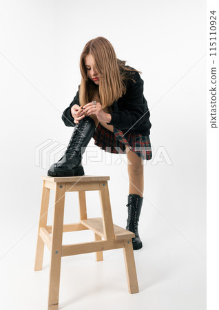 Teenage girl tying shoelaces on white background. Teenager girl in a skirt posing in the studio on a white background. Teenage girl tying shoelaces on white background. Teenager girl in a skirt posing in the studio on a white background. 115110924