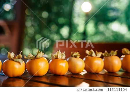 Ripe yellow persimmon lined up in a row lies on a wooden table in the gazebo Ripe yellow persimmon lined up in a row lies on a wooden table in the gazebo 115111104