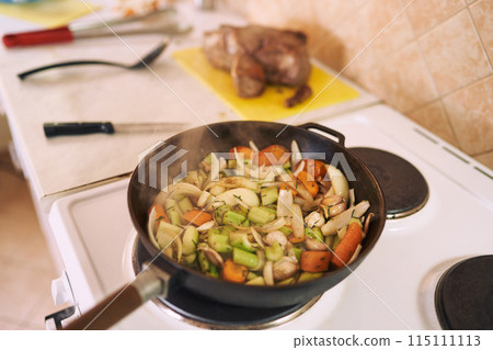 Steam rises from chopped vegetables stewed in a frying pan on the stove 115111113
