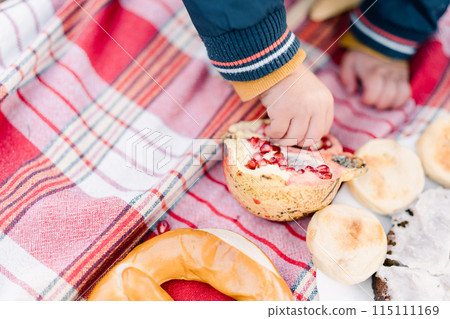 Small child picks out seeds from a pomegranate while sitting on a bedspread. Cropped. Faceless Small child picks out seeds from a pomegranate while sitting on a bedspread. Cropped. Faceless 115111169