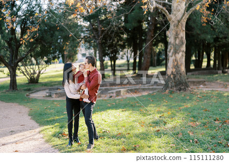 Mom hugs dad with a little girl in his arms kissing her on the cheek Mom hugs dad with a little girl in his arms kissing her on the cheek 115111280