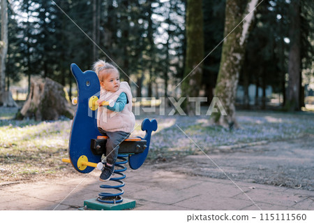 Little girl sits on a spring swing and looks away Little girl sits on a spring swing and looks away 115111560