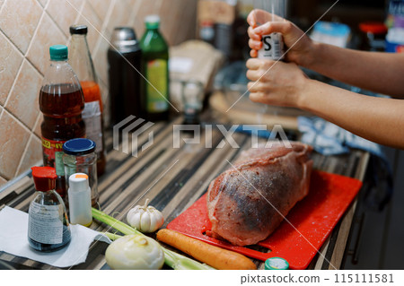 Cook sprinkles a piece of tenderloin on a cutting board with spices from a glass mill 115111581