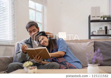 Elderly couple reading book together on couch, Concept of companionship and love Elderly couple reading book together on couch, Concept of companionship and love 115111582