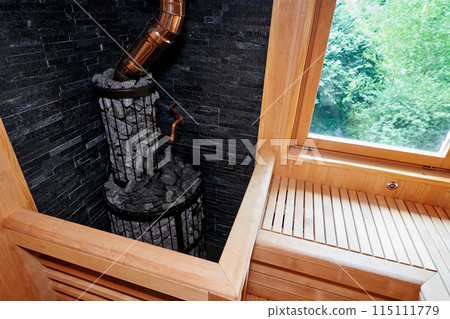 Metal stove filled with stones with a pipe in a wooden sauna 115111779