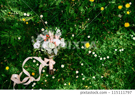 Bridal bouquet lies on a green lawn among wildflowers. Top view 115111797