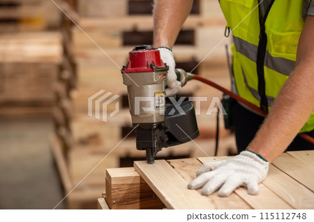 Engineer carpenter wearing safety uniform and yellow hard hat working using electric nail gun 115112748
