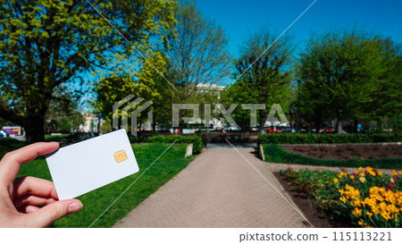 A person is holding a white credit card in a park A person is holding a white credit card in a park 115113221