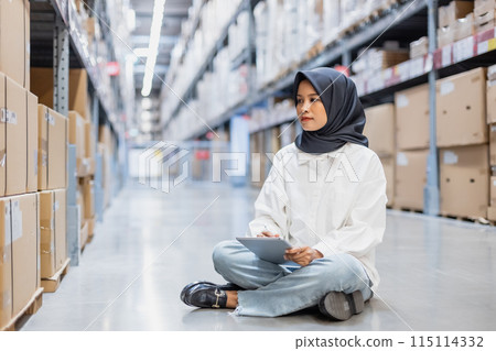 Muslim female wearing hijab warehouse worker holding tablet checks stock on shelf storehouse. 115114332