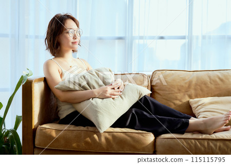 A woman relaxing on a sofa while basking in the morning sun 115115795
