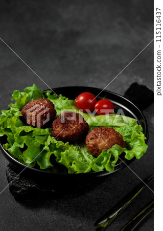 Fried cutlets on a lettuce leaf with tomato on a black background Fried cutlets on a lettuce leaf with tomato on a black background 115116437