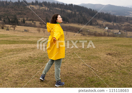 hiking, young woman in a yellow raincoat in the mountains 115118083