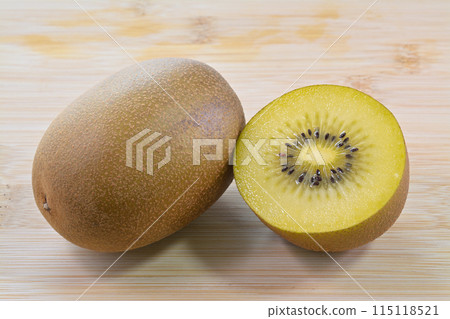 Gold kiwi fruit cut in half on a cutting board 115118521