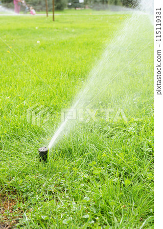 Automatic smart lawn sprinkler with adjustable head watering green lawn grass in sunny day 115119381