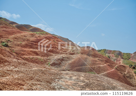 Hills of vibrant red hues under blue spring skies, the colorful terrain creates a picturesque and serene alien landscape Hills of vibrant red hues under blue spring skies, the colorful terrain creates a picturesque and serene alien landscape 115119626