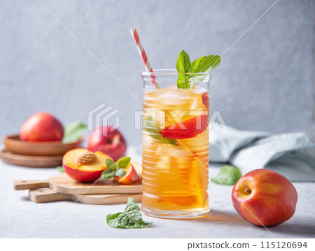 cool peach tea with mint and ice in a glass on a blue background. Front view and copy space cool peach tea with mint and ice in a glass on a blue background. Front view and copy space 115120694