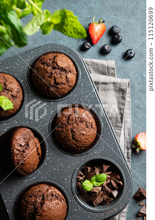chocolate muffins with blueberry and strawberry slices in a baking dish on a dark background. chocolate muffins with blueberry and strawberry slices in a baking dish on a dark background. 115120699