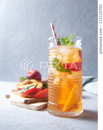 cool peach tea with mint and ice in a glass on a blue background. Front view and copy space cool peach tea with mint and ice in a glass on a blue background. Front view and copy space 115120702
