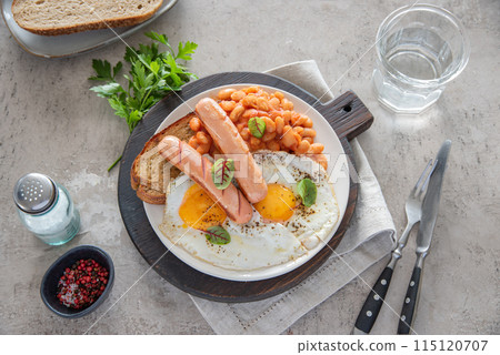 Traditional English breakfast with fried eggs, sausages, beans, fresh herb, red pepper and toast Traditional English breakfast with fried eggs, sausages, beans, fresh herb, red pepper and toast 115120707