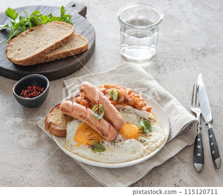 Traditional English breakfast with fried eggs, sausages, beans, fresh herb, red pepper and toast Traditional English breakfast with fried eggs, sausages, beans, fresh herb, red pepper and toast 115120711