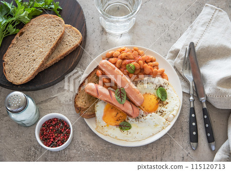 Traditional English breakfast with fried eggs, sausages, beans, fresh herb, red pepper and toast Traditional English breakfast with fried eggs, sausages, beans, fresh herb, red pepper and toast 115120713