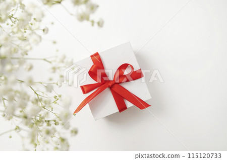 a white gift box with a red ribbon on a white background with a bouquet of  gypsophila.  115120733