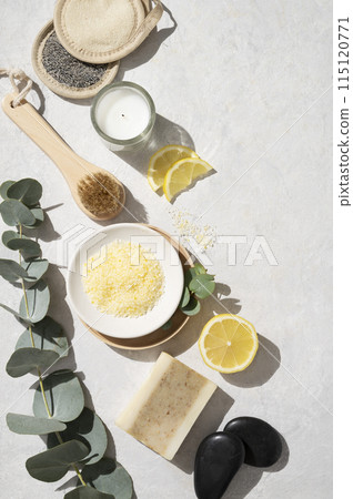 Flat lay organic yellow sea salt with lemon, soap, massage stone, sponge and eucalyptus branch 115120771