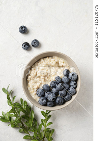 Oatmeal porridge with blueberries in bowl on a blue background with branch.  115120778