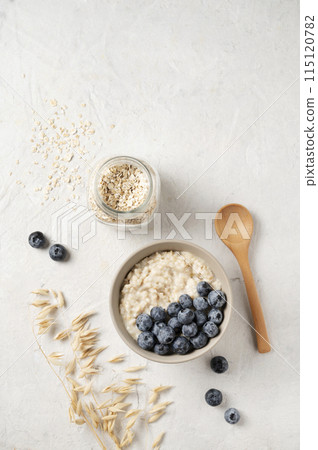 Oatmeal porridge with blueberries in bowl with wooden spoon and jar of oats flakes Oatmeal porridge with blueberries in bowl with wooden spoon and jar of oats flakes 115120782