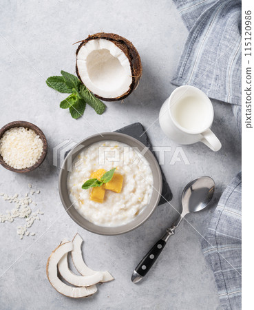 Rice porridge with coconut milk and mango slices in bowl on a blue background. 115120986