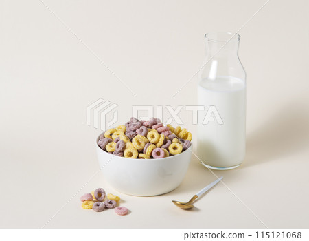 sweet colorful cornflakes rings in a white bowl with spoon and a bottle of milk  115121068