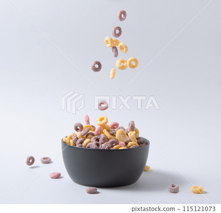 sweet colorful cornflakes rings fly in a black bowl on gray background. Front view and copy space sweet colorful cornflakes rings fly in a black bowl on gray background. Front view and copy space 115121073