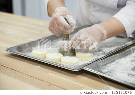 A woman makes cheesecakes by hand in production. Factory for the production of food. 115121076