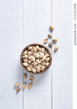 Pistachio nuts in a brown bowl on a white wooden background. Top view and copy space 115121098