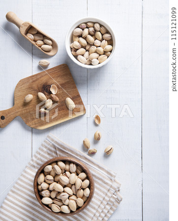 Flat lay pistachio nuts in bowls, on a cutting board and in a spoon on a white wooden background. 115121099