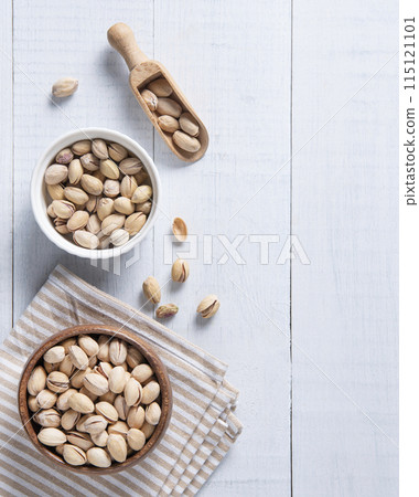 Flat lay pistachio nuts in bowls, on a cutting board and in a spoon on a white wooden background. Flat lay pistachio nuts in bowls, on a cutting board and in a spoon on a white wooden background. 115121101
