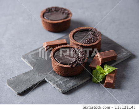 mini chocolate tarts with piece chocolate and mint on a gray background mini chocolate tarts with piece chocolate and mint on a gray background 115121145