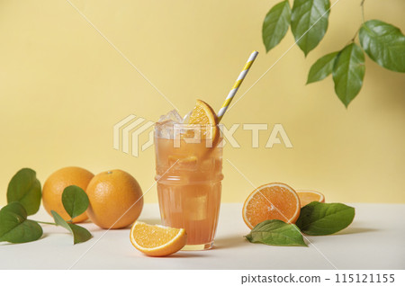 A glass of refreshing orange juice with a slice of orange and ice on a yellow background A glass of refreshing orange juice with a slice of orange and ice on a yellow background 115121155
