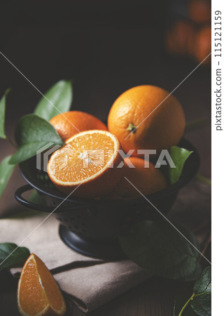 A few juicy oranges in a black bowl with green leaves on a dark wooden background. A few juicy oranges in a black bowl with green leaves on a dark wooden background. 115121159