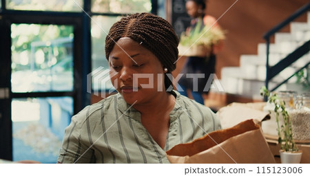 Buyer enjoying fresh smell of locally grown lemons from farm, smelling citric aroma and putting ecological fruits in a bag. African american client looking for homegrown goods. Tripod shot. 115123006