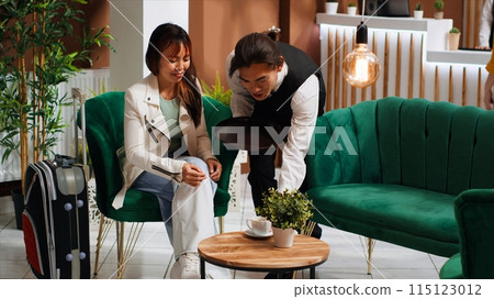 Professional waiter serving coffee for asian client at hotel, ensuring pleasant stay for guest and offering great customer service. Young man bringing drink to lounge area for tourist. 115123012