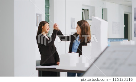 Designers give a high five after drafting objectives, satisfied with their efforts in converting dimensions and deciding scaling components for construction. Women finish assignments correctly. 115123116