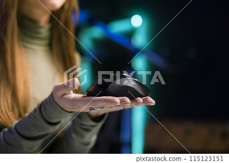 Woman filming video for online channel in dimly lit home studio, presenting wireless mouse to fans. Content creator showing audience computer peripheral device, close up shot 115123151