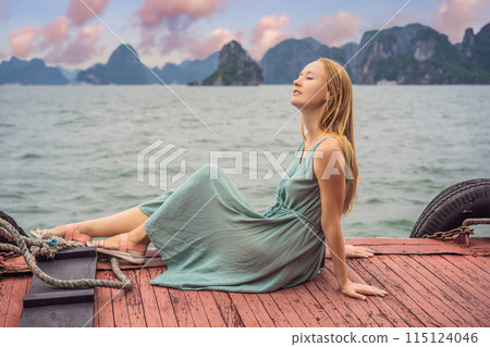 Attractive woman in a dress is traveling by boat in Halong Bay. Vietnam. Travel to Asia, happiness emotion, summer holiday concept. Picturesque sea landscape. Ha Long Bay, Vietnam Attractive woman in a dress is traveling by boat in Halong Bay. Vietnam. Travel to Asia, happiness emotion, summer holiday concept. Picturesque sea landscape. Ha Long Bay, Vietnam 115124046