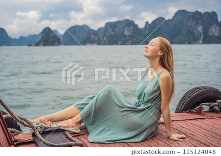 Attractive woman in a dress is traveling by boat in Halong Bay. Vietnam. Travel to Asia, happiness emotion, summer holiday concept. Picturesque sea landscape. Ha Long Bay, Vietnam 115124048
