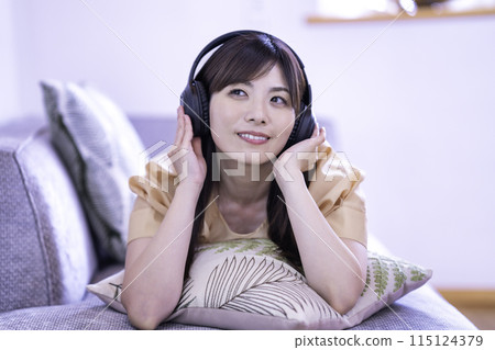 Woman lying on the sofa and listening to music 115124379