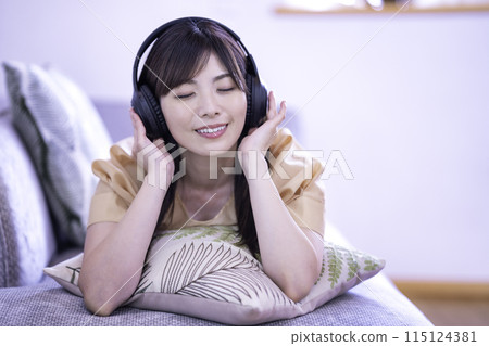 Woman lying on the sofa and listening to music Woman lying on the sofa and listening to music 115124381