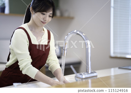 A housewife wearing an apron doing the washing up 115124916