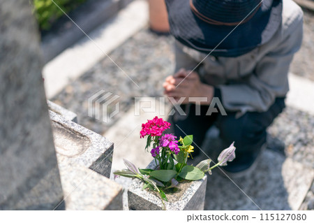 Senior woman praying to the grave with her hands together in front of the grave 115127080