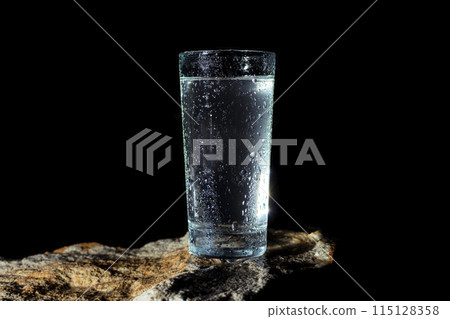 a glass of water with walls fogged up from the cold on a rock on a black background a glass of water with walls fogged up from the cold on a rock on a black background 115128358